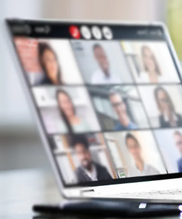 Person arbeitet am Laptop und nimmt an einer Videokonferenz mit mehreren Teilnehmenden teil – modernes Remote‑Work‑ und Teamwork‑Setting.