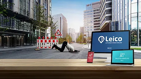 Holztisch mit Monitor, Tablet und Smartphone, die Leico‑Oberflächen zeigen. Dahinter eine städtische Straße mit Baustellenabsperrung und einer Person, die in ein Loch gestürzt ist.