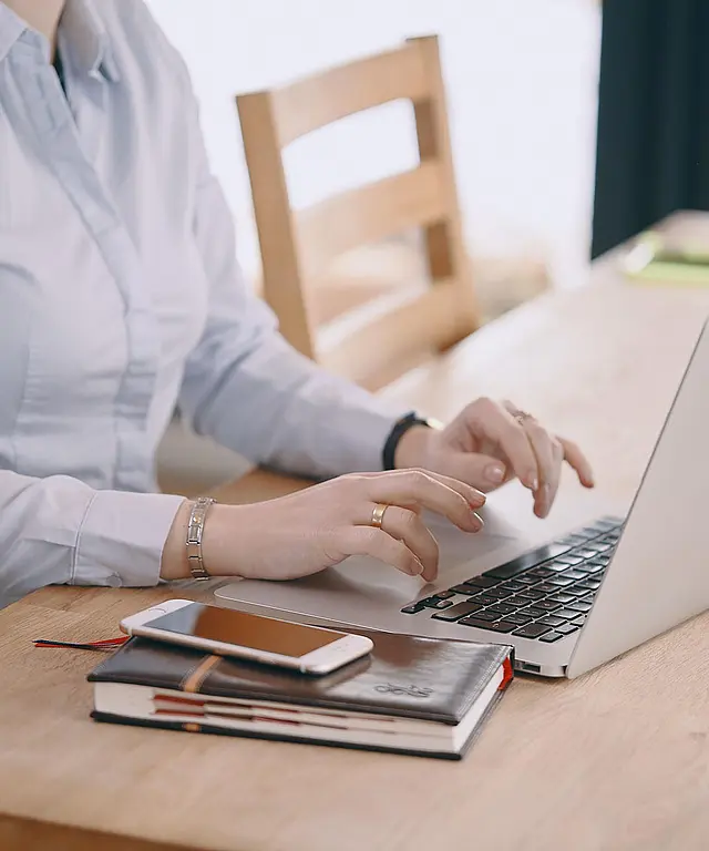 Junge Frau sitzt an einem Schreibtisch und arbeitet konzentriert an einem Laptop in einem modernen Büro.