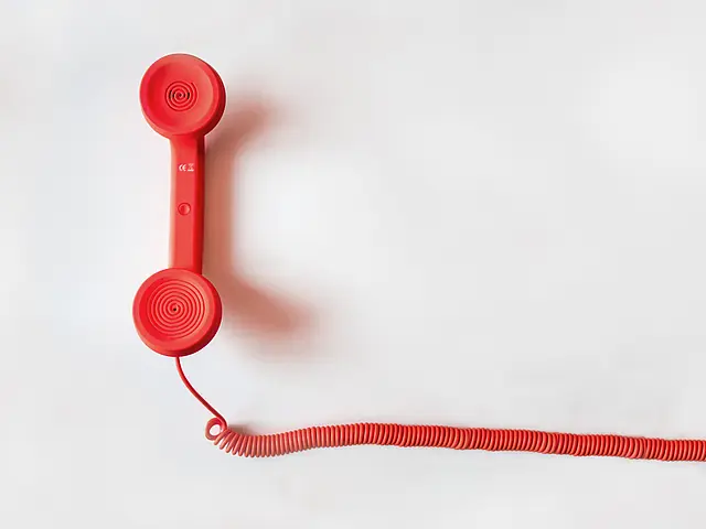 Roter, klassischer Telefonhörer liegt mit langem Spiralkabel auf einer hellen Fläche; minimalistische, klare Draufsicht.