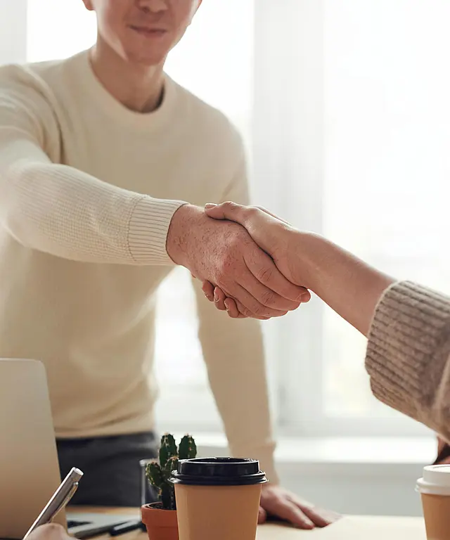 Zwei Menschen geben sich im Büro die Hand. Symbolbild für Zusammenarbeit, Einigung und erfolgreiche Gespräche.