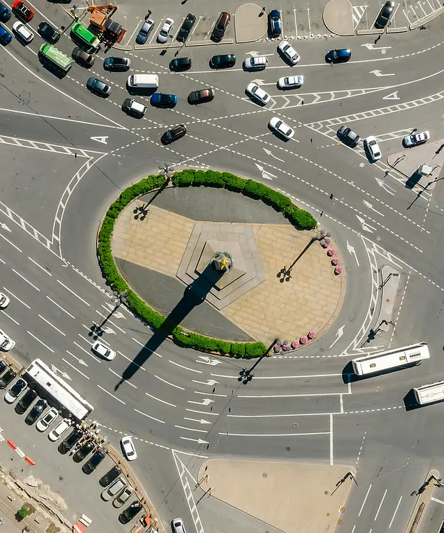 Luftaufnahme eines großen Verkehrsknotpunkts mit vielen Spuren und Fahrzeugen. Zentraler Rundplatz mit Denkmal, urbaner Verkehrsfluss von oben.